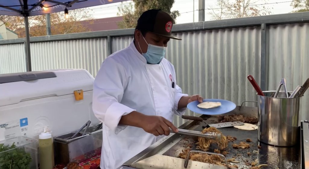 A chef flips meat on the grill in an outdoor kitchen.