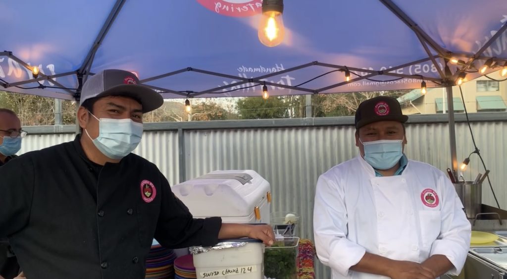 Two chefs standing side by side in their outdoor catering kitchen.