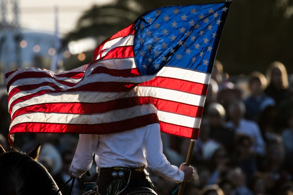 Megan sharp tucks the pole of the american flag in her cowgirl boot to keep it stable while she sits atop her horse. 