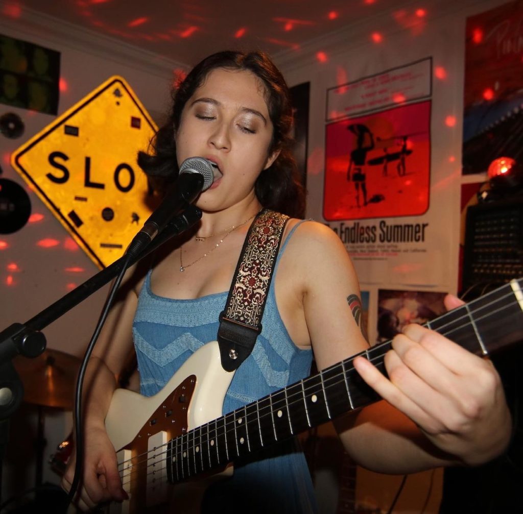 Amanda Mei plays guitar and sings into a microphone.