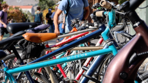 There are many bikes parked at a bike rack on Cal Poly's campus. In the background a man is seen parking his bike.