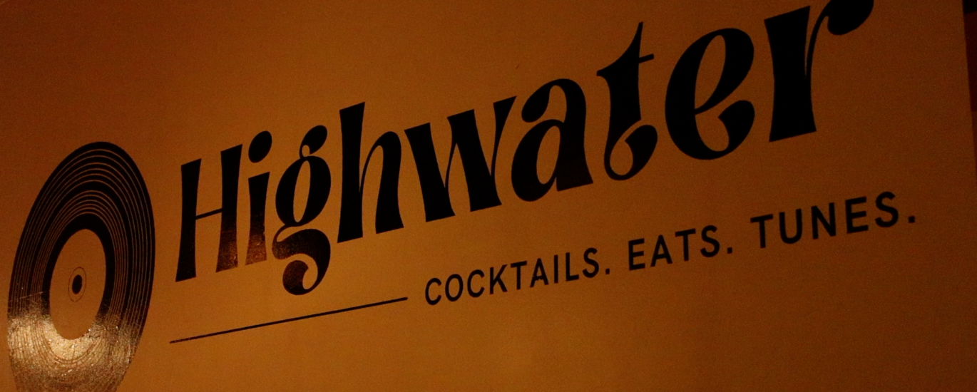 A wall is pictured with the word “Highwater” is a bold font. Under this title are the words “Cocktails. Eats. Tunes.” in all capital letters. A drawing of a record is seen on the left of the text.